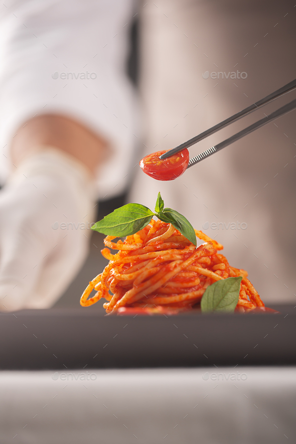 A chef in a white uniform and gloves decorates pasta in tomato sauce